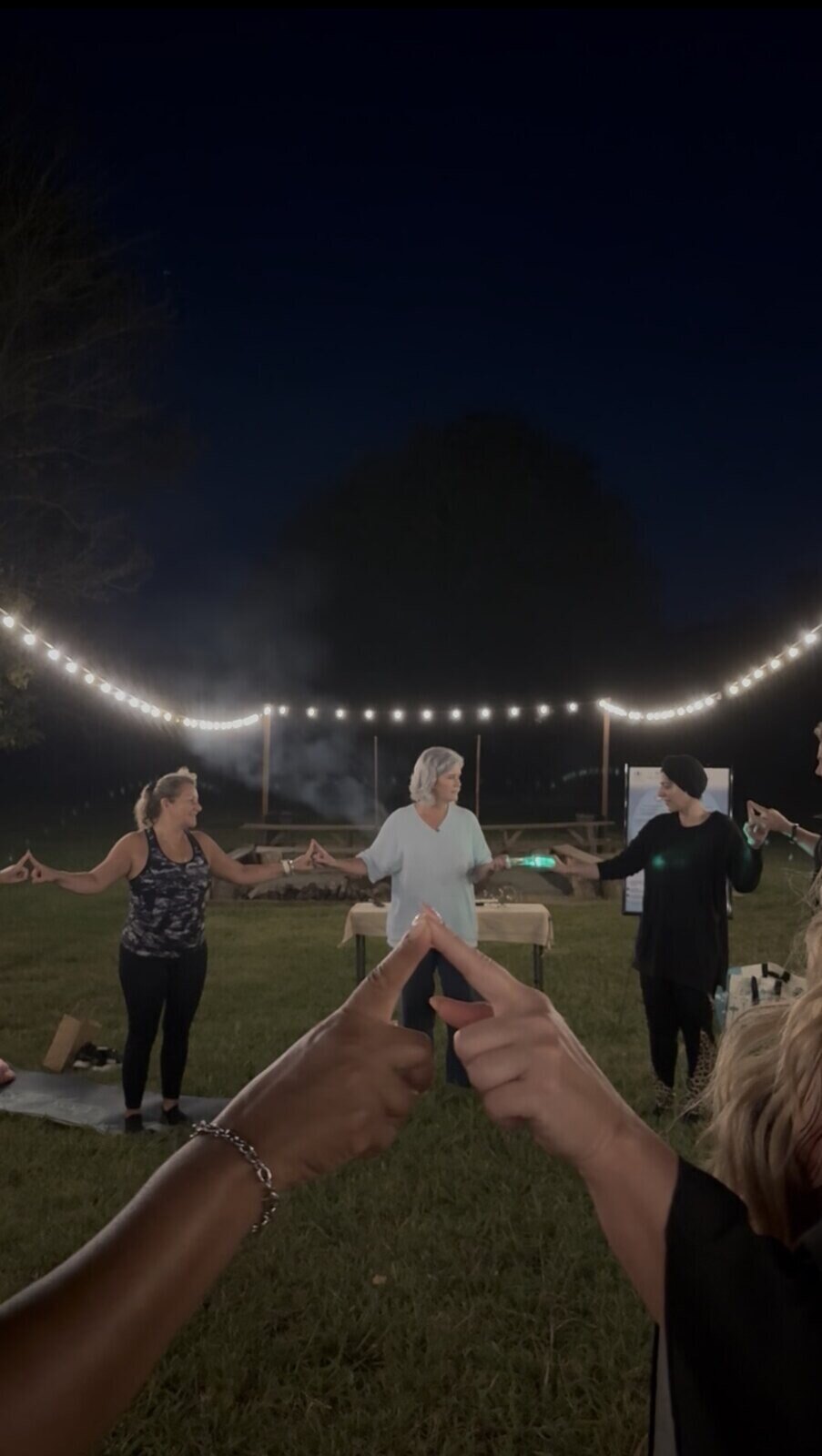 A community circle connected beneath string lights after sunset
