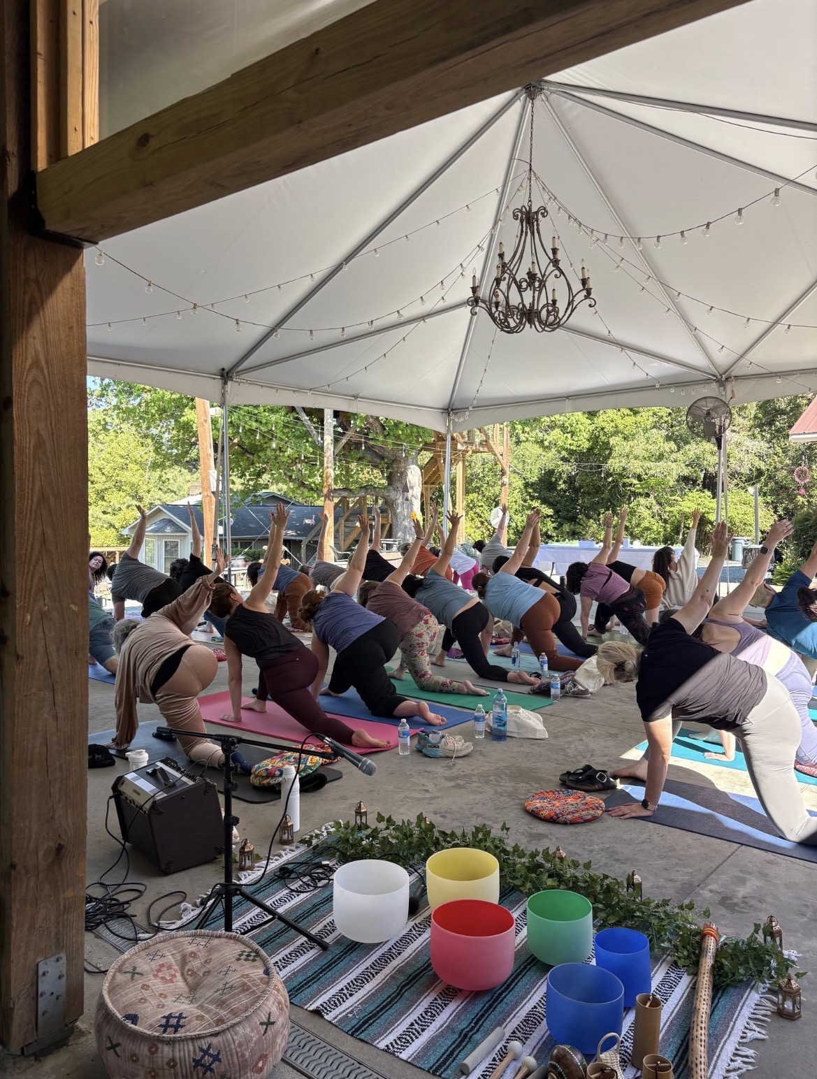 A full group of RETURN guests moving together in a grounded arm-up twist beneath the pavilion